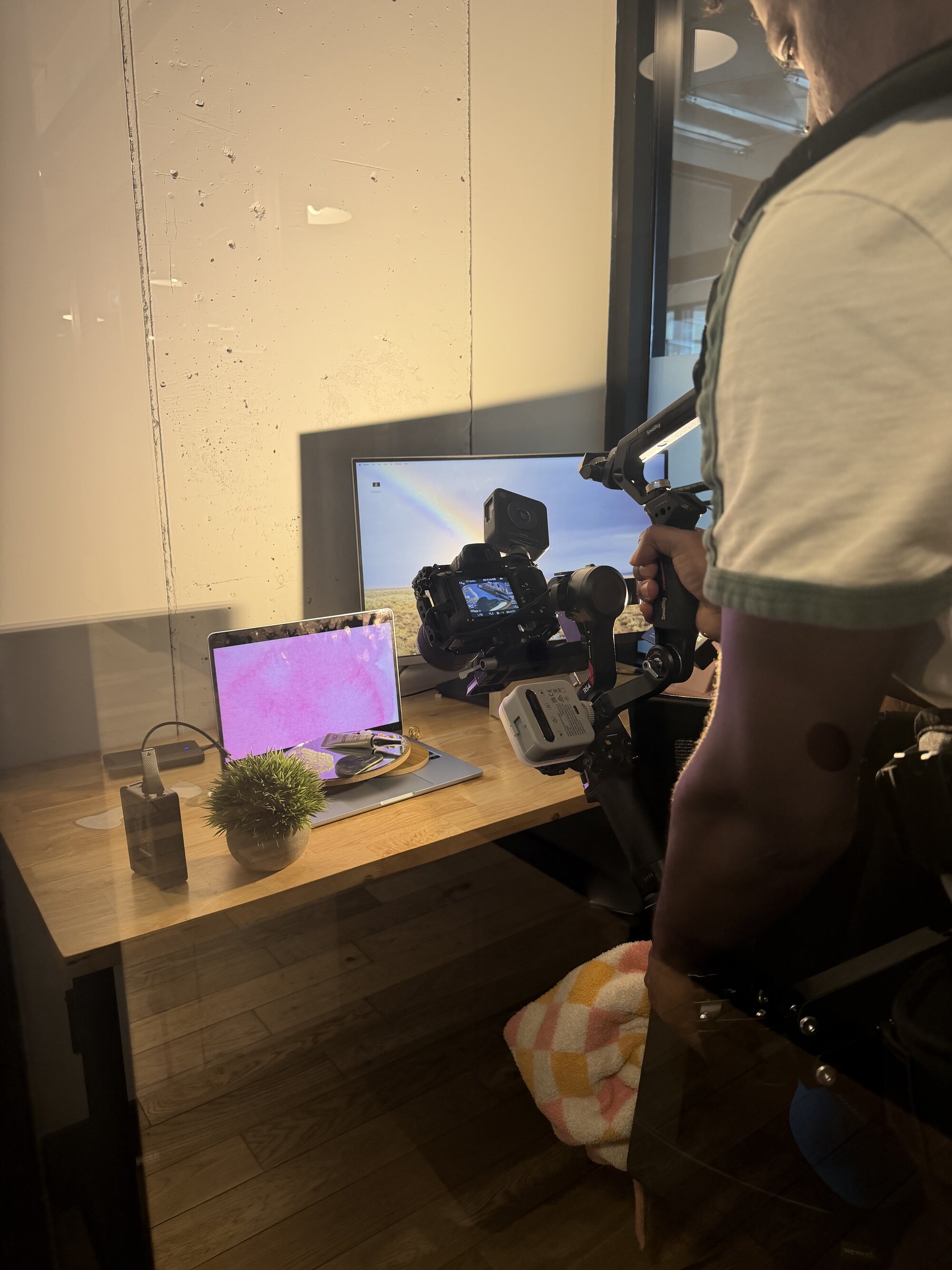 A TNAADO operator on a gimbal and body rig filming a built product set on a desk, with the client's screens lit behind it.