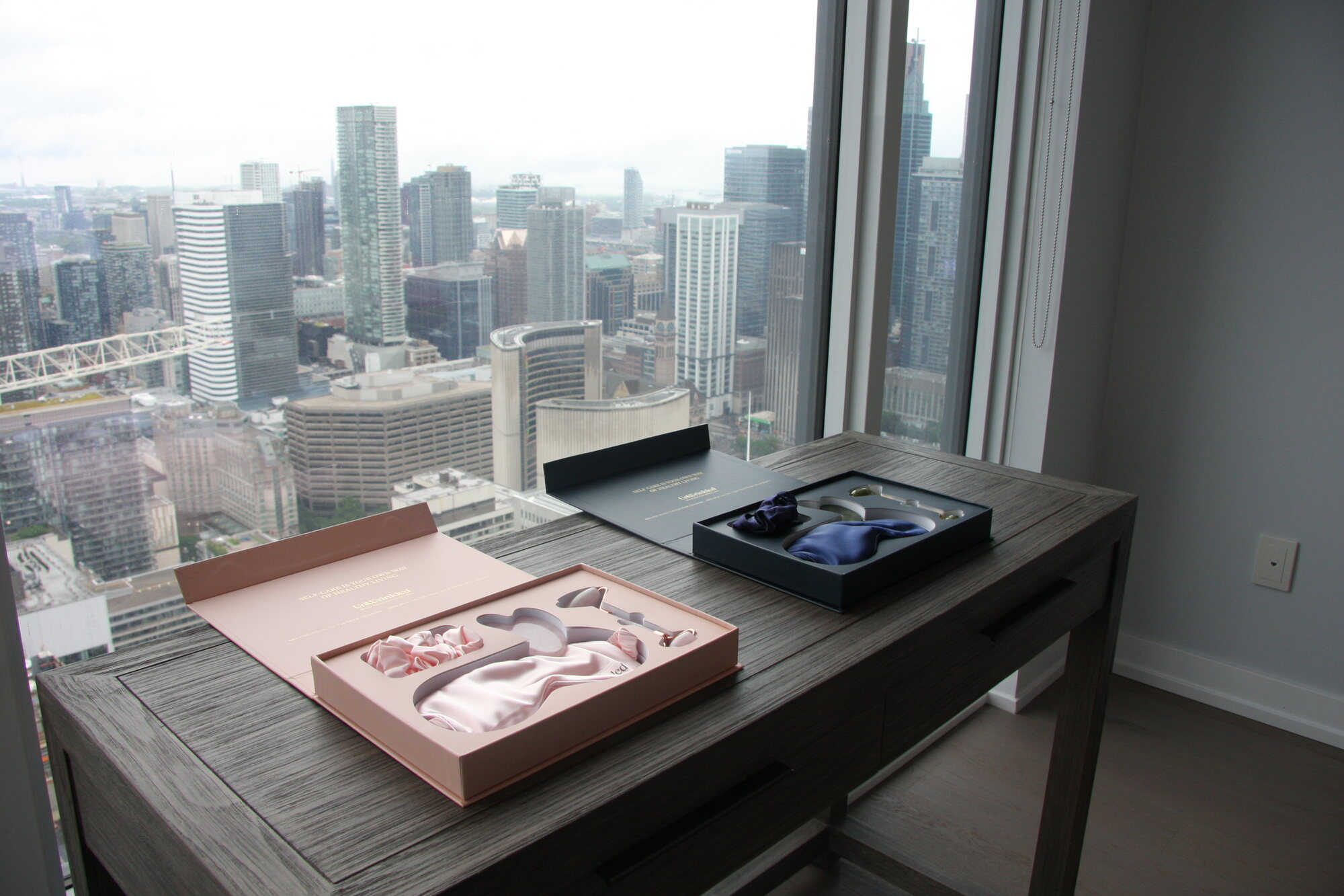 Two open UnWrinkled gift boxes staged on a desk in a high-floor Toronto condominium, with the downtown skyline filling the window behind them.