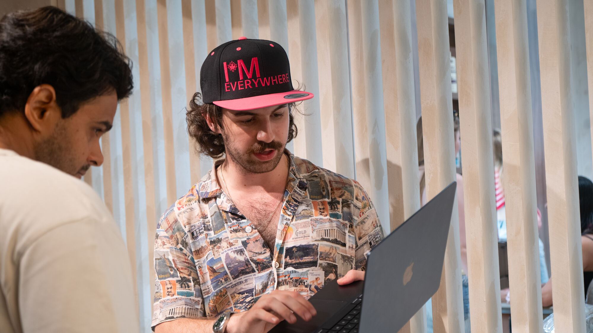 A TNAADO founder standing with a laptop, talking a client through software running on screen; the client listens in the foreground.